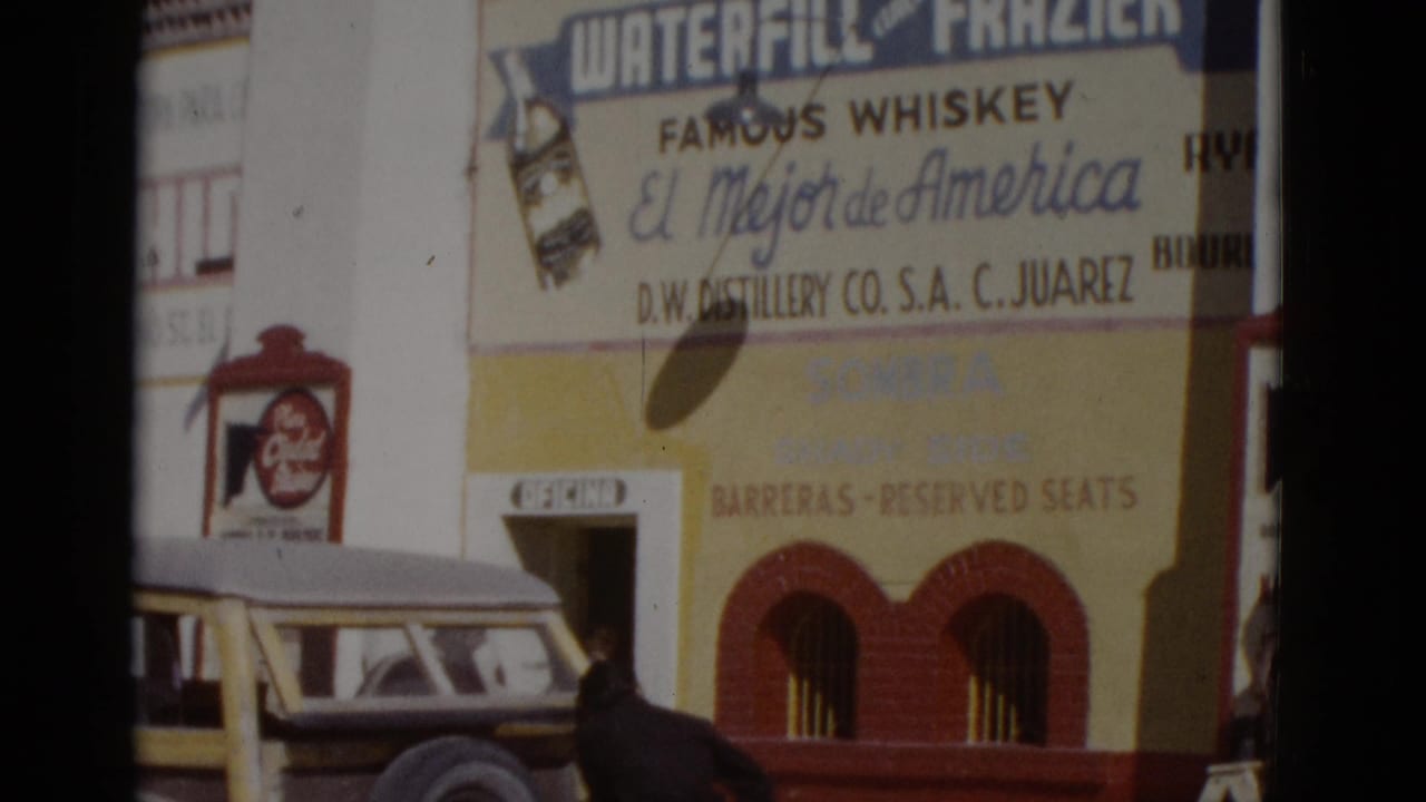 Building facade displaying 'Waterfill & Frazier Famous Whiskey / El Mejor de America' sign with a parked vintage vehicle, likely northern Mexico, c.1952.
