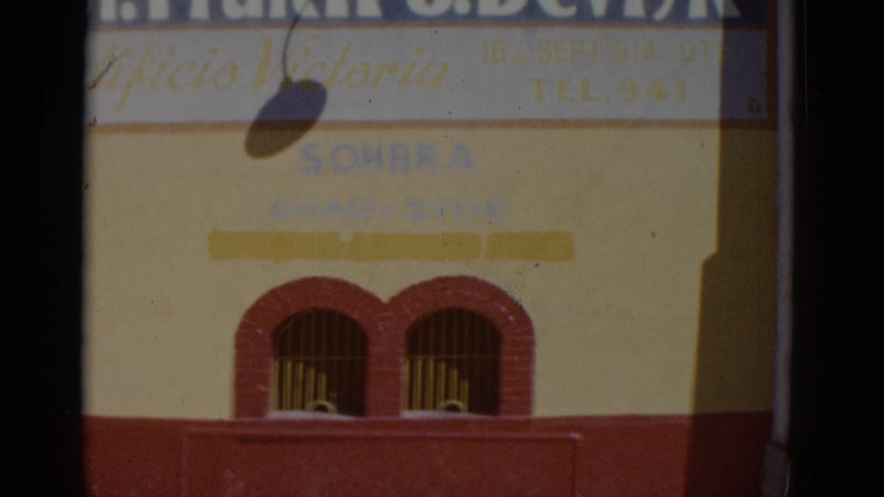 Static repeat shot of the Devlyn Edificio Victoria building facade in Baja California, circa 1952; yellow stucco with red trim and hand-lettered commercial signage.