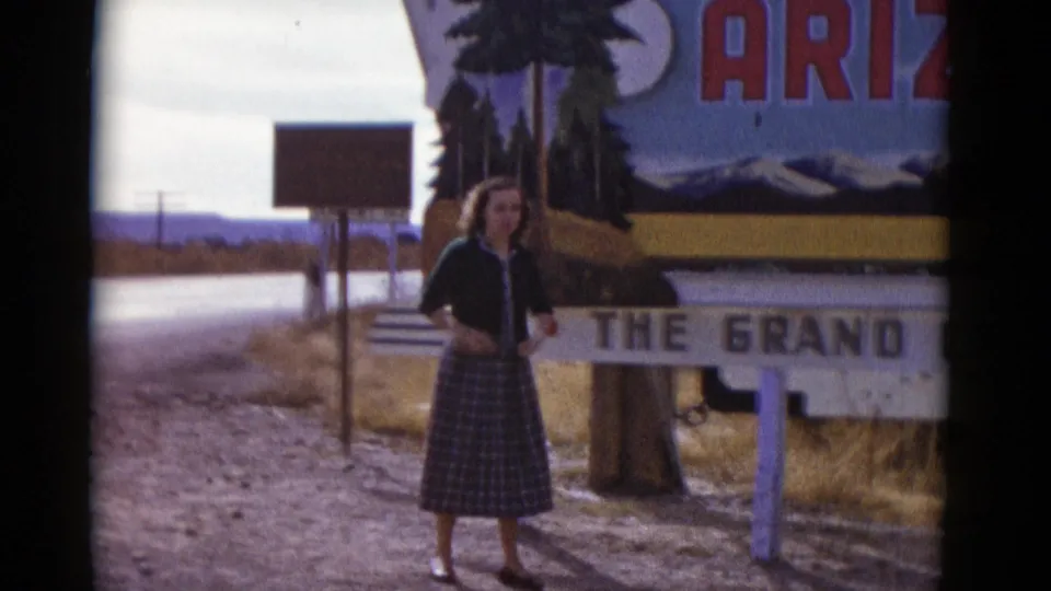 1952 home-movie frame of a woman posing beside a large Grand Canyon roadside sign in Baja California, Mexico.
