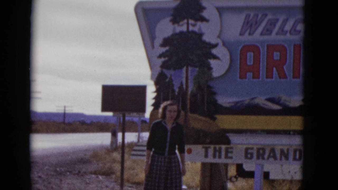 Woman standing beside a large Welcome to Arizona sign on a roadside.