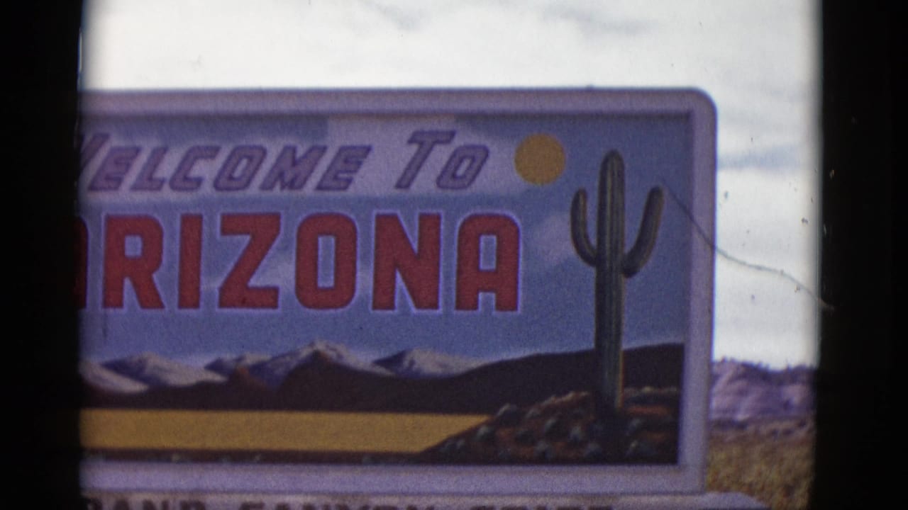 1952 Arizona frame with the right side of a Welcome to Arizona sign, showing cactus artwork, red lettering, a sun symbol, and painted desert-mountain imagery.
