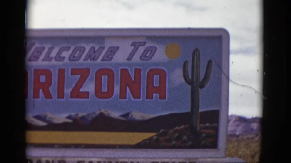 1952 Arizona frame with the right side of a Welcome to Arizona sign, showing cactus artwork, red lettering, a sun symbol, and painted desert-mountain imagery.