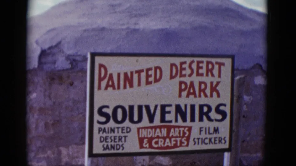 1952 Arizona frame showing the Painted Desert Park Souvenirs sign against a rough wall, with smaller text for painted desert sands, Indian arts and crafts, and film stickers.