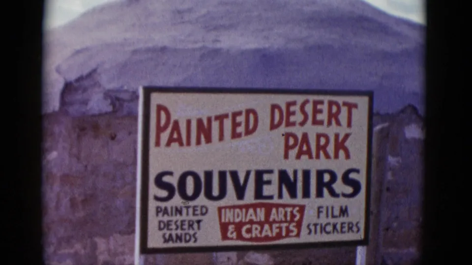 1952 Arizona home-movie frame showing a Painted Desert Park souvenir sign against rugged desert formations.