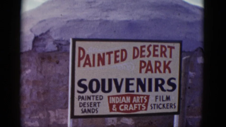 1952 Arizona travel footage frame with a roadside Painted Desert Park souvenir sign and rocky terrain behind it.