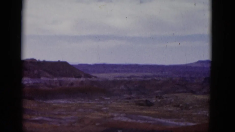 1952 Arizona 8mm frame showing an open desert valley, low hills, distant mesa, muted sky, and visible film gate edges.