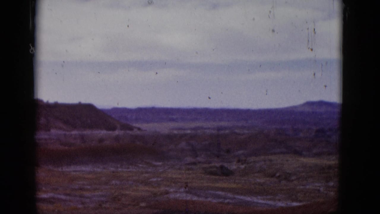 Desert panorama with low ridges, broad arid ground, pale sky, and central film divider.