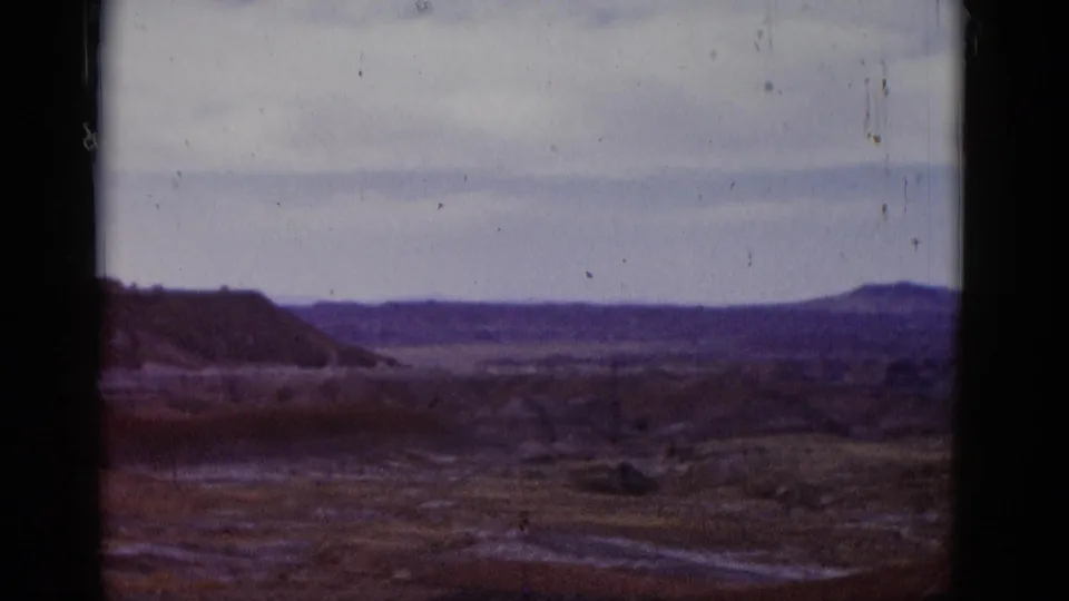 1952 Arizona travel frame with a wide desert view, low ridges, open arid ground, pale sky, and physical film border visible.