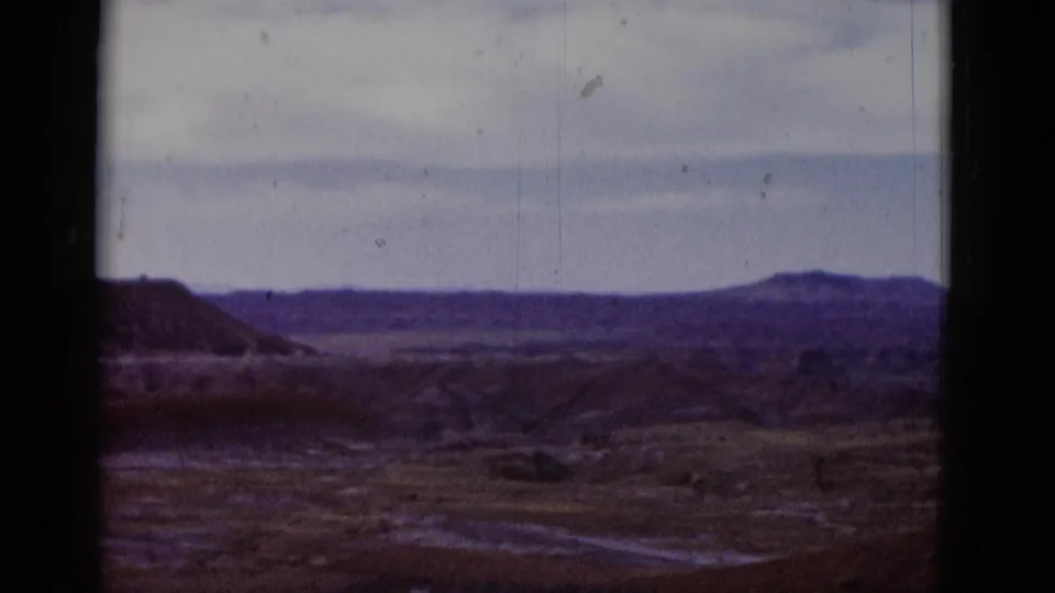 1952 Arizona 8mm frame showing desert flats, low hills, a distant ridge line, pale sky, scratches, and dust on the film.