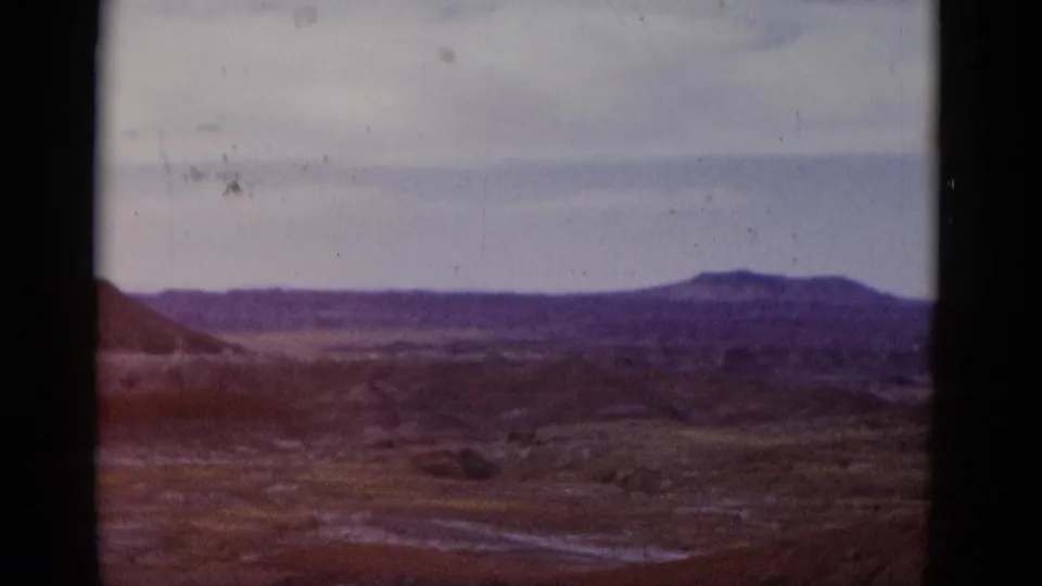 1952 Arizona home-movie frame with a distant mound-like hill, scrubby desert terrain, pale sky, warm fading color, and film grain.