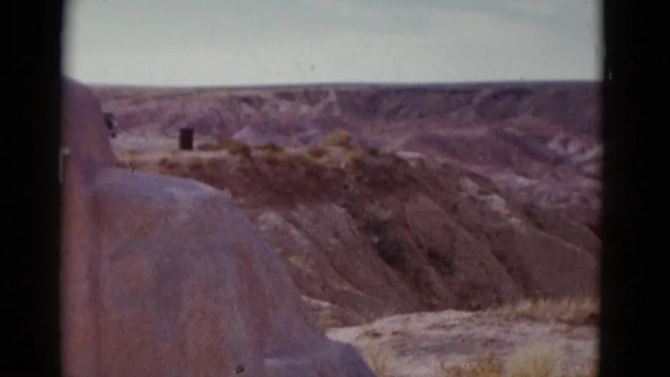 1952 Arizona home-movie frame looking past a cropped stone marker toward layered canyon walls and sparse desert vegetation.
