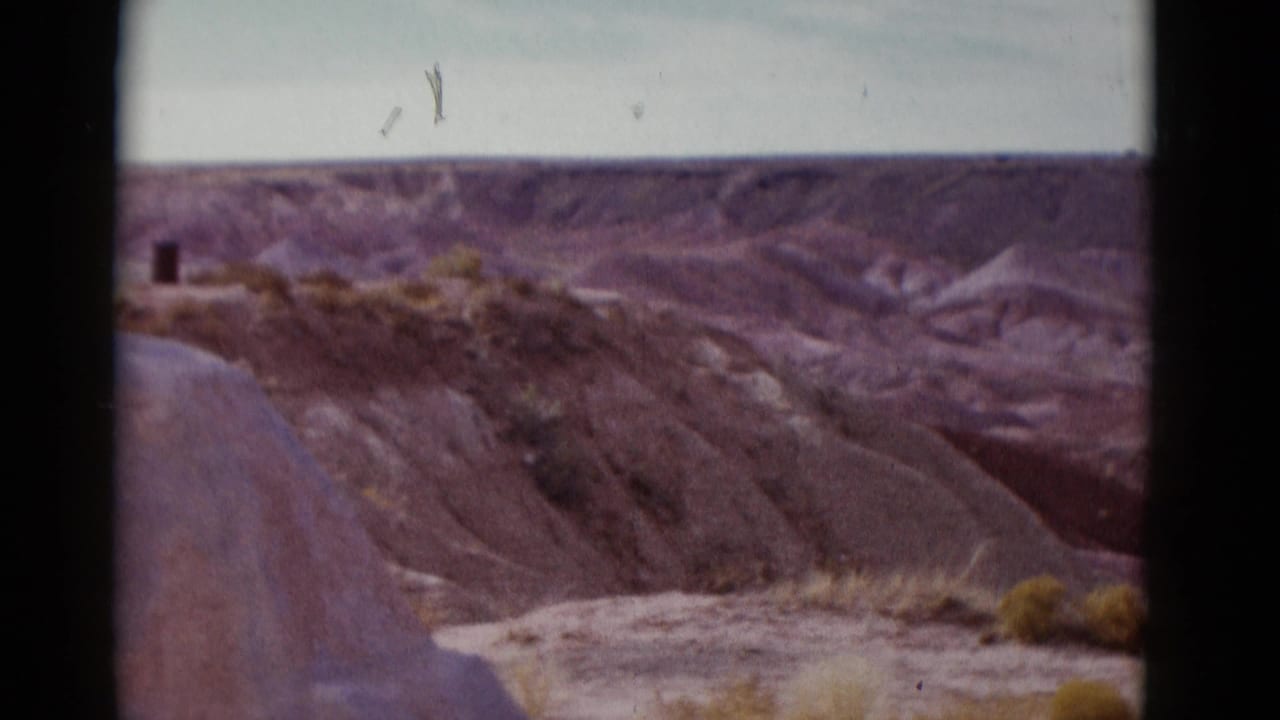 Reddish desert ridges and dry foreground ground seen through a dark film gate border.