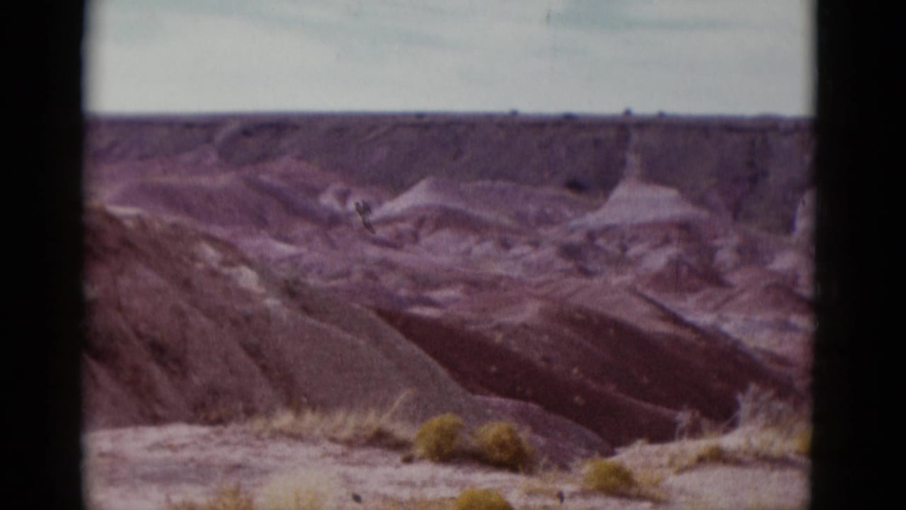 1952 Arizona home-movie frame showing eroded desert badlands, low shrubs, and a pale horizon in soft 8mm color.