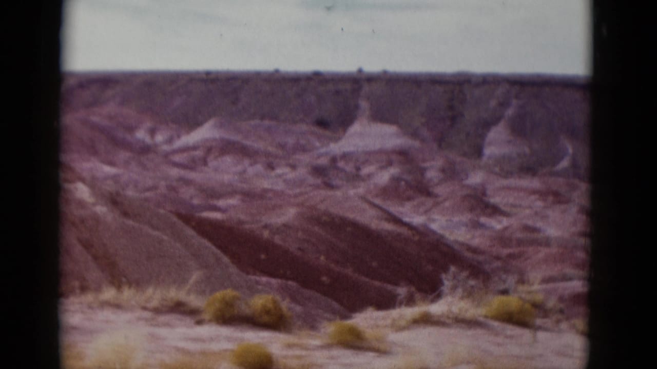 Desert ravines and rounded rock formations with low scrub near the foreground edge.