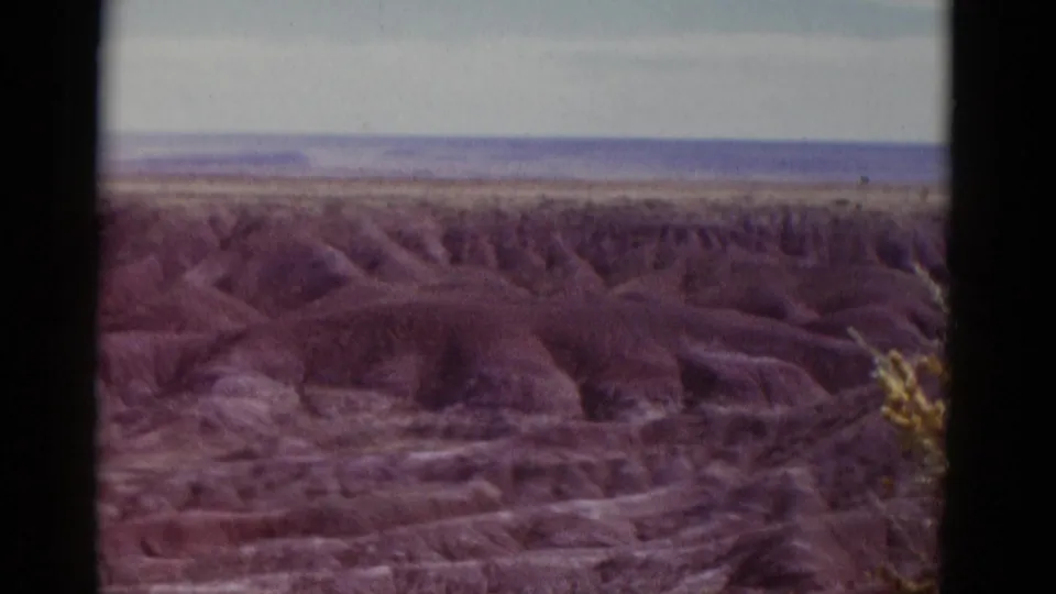Wide 1952 Arizona desert view with distant plateau-like horizon, eroded hills, and soft faded 8mm color.
