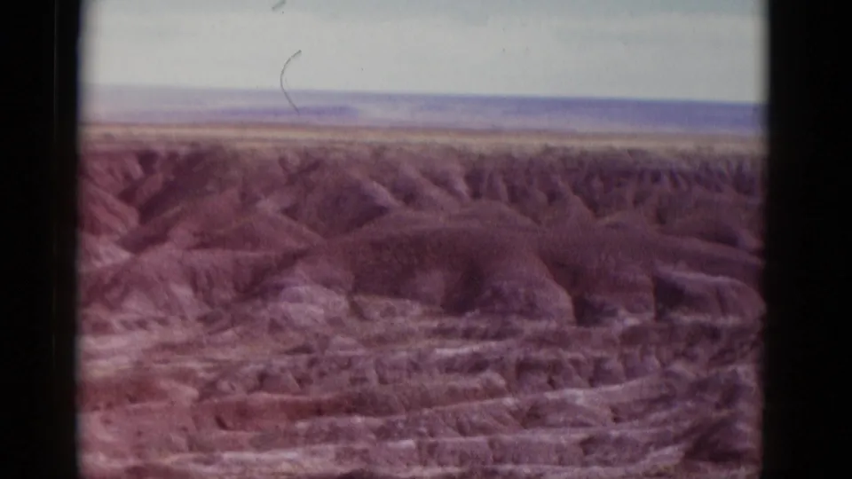 1952 Arizona 8mm frame showing open desert badlands, a pale skyline, sparse vegetation, and visible film-frame borders.