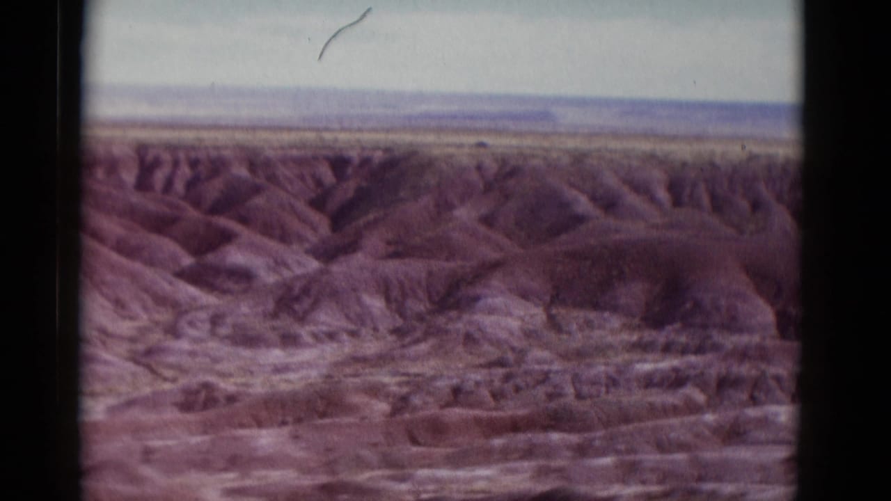 1952 Arizona 8mm travel view of ridged desert terrain and canyon-like washes under a pale sky, framed by the scanned film edge.