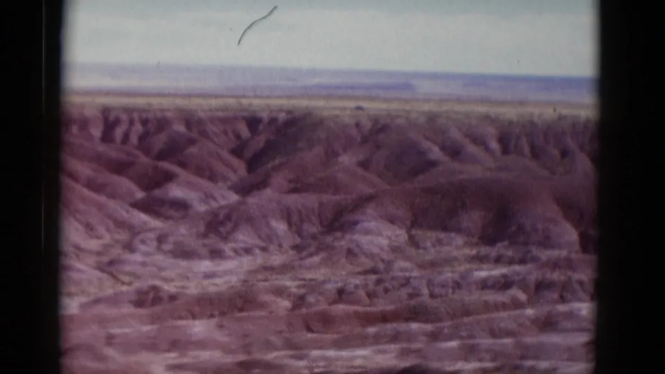 1952 Arizona 8mm travel view of ridged desert terrain and canyon-like washes under a pale sky, framed by the scanned film edge.