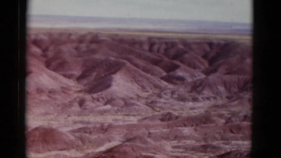 1952 Arizona 8mm frame showing a closer portion of rugged desert hills and dry washes, with faded color and dark film borders from the scan.