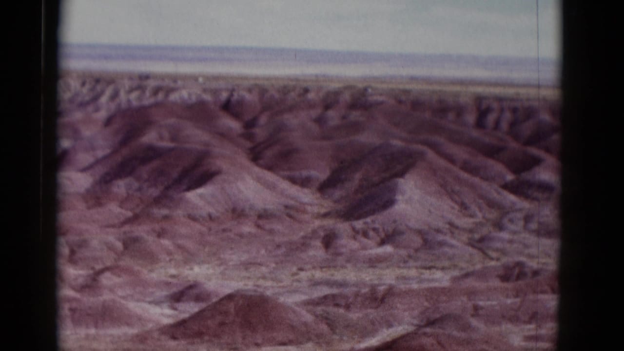 Wide view of layered desert ridges and rounded hills under a pale sky.