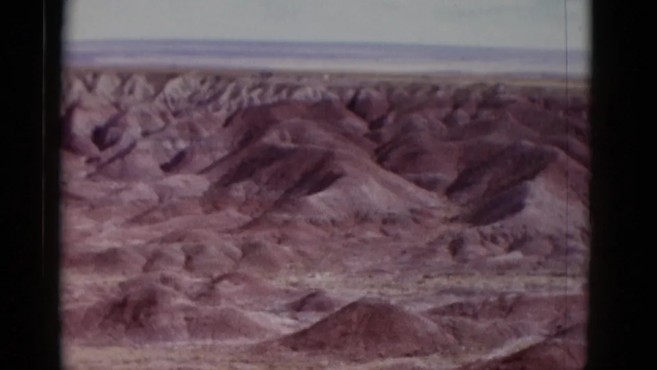 1952 Arizona 8mm frame showing reddish-brown rolling desert mounds, shallow gullies, and distant badland-like ridges.