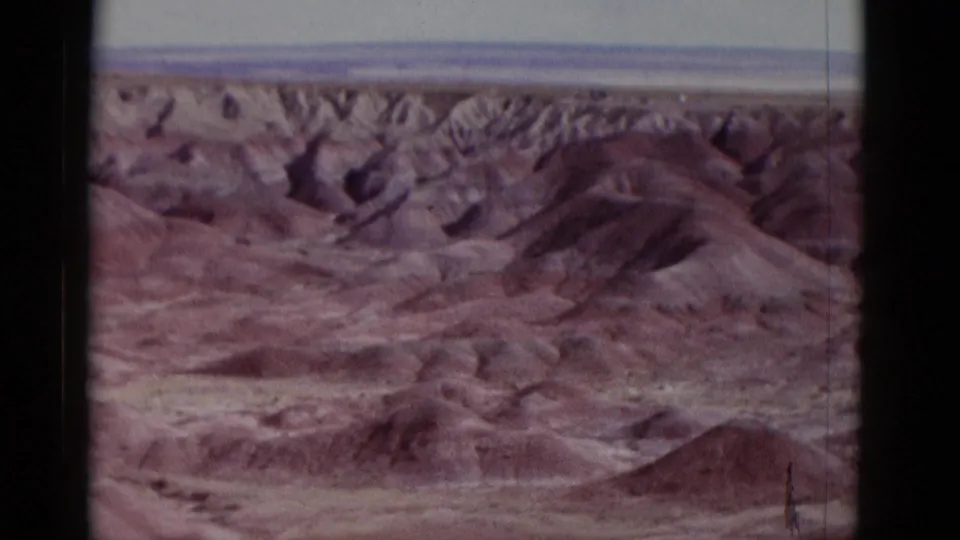 1952 Arizona 8mm frame with eroded desert ridges, low reddish hills, gullies, and a pale sky beyond.