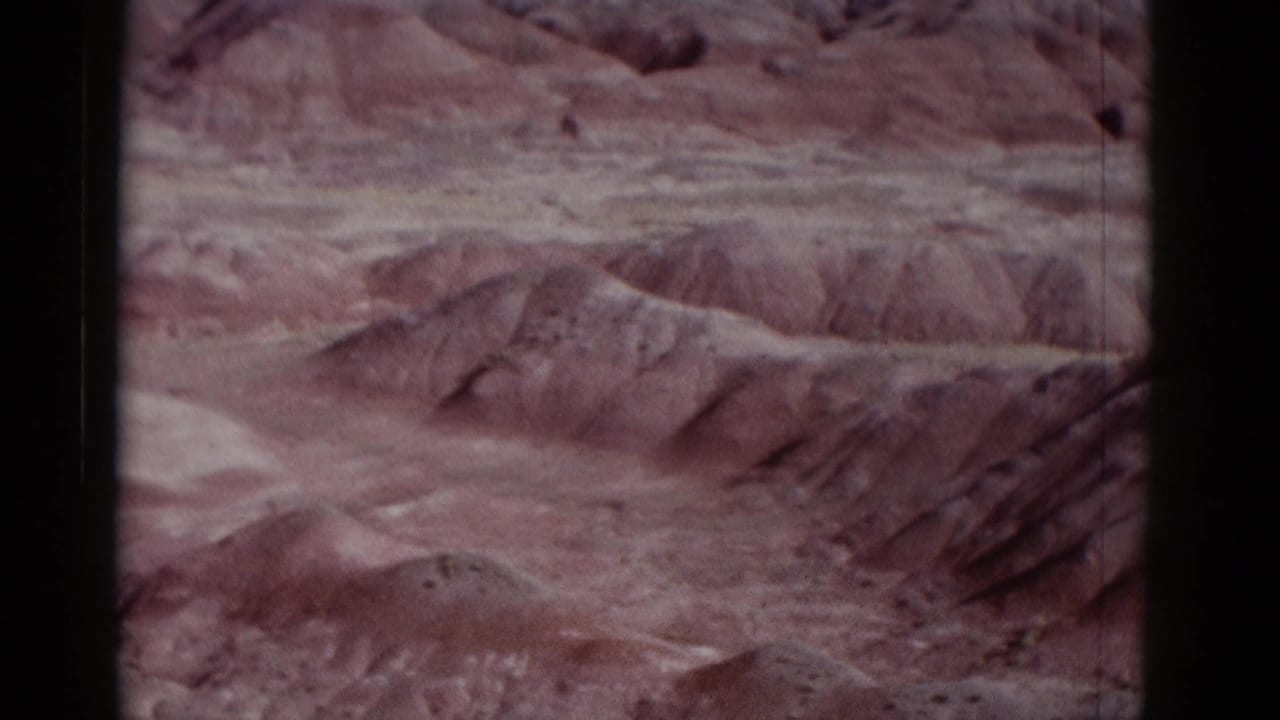 Rounded desert ridges and dry washes under a pale sky, with film scratches visible.