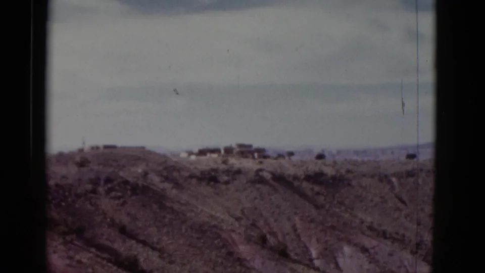 1952 home-movie view across eroded Arizona desert terrain toward small distant buildings on a ridge.