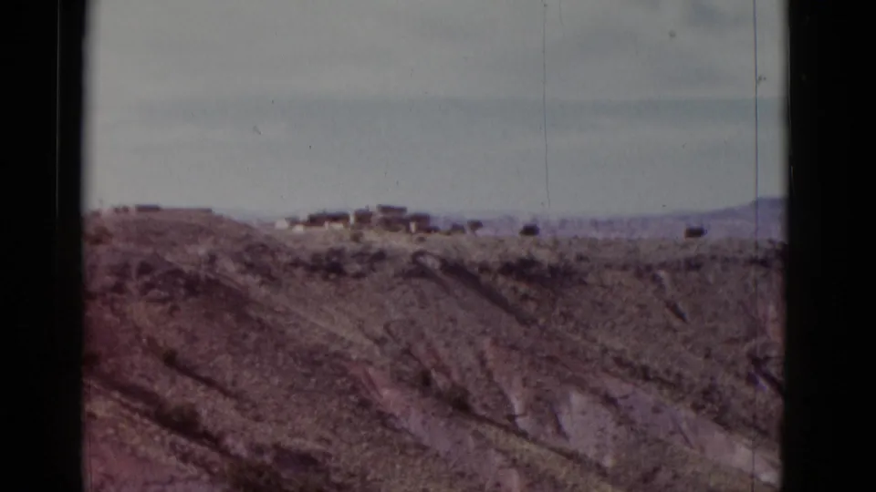 Faded 8mm frame showing a far desert ridge with small buildings and eroded Arizona canyon slopes below.