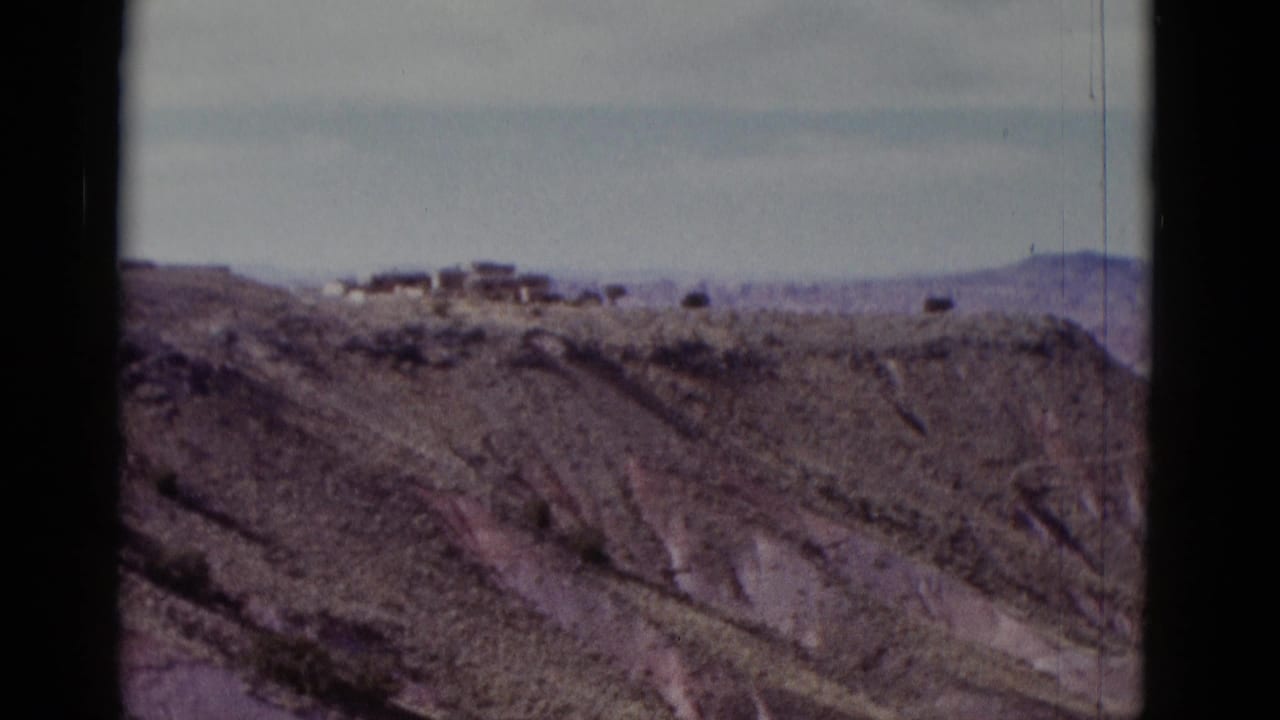1952 Arizona 8mm frame showing a rugged layered hillside, sparse vegetation, and small distant ridge-top structures.