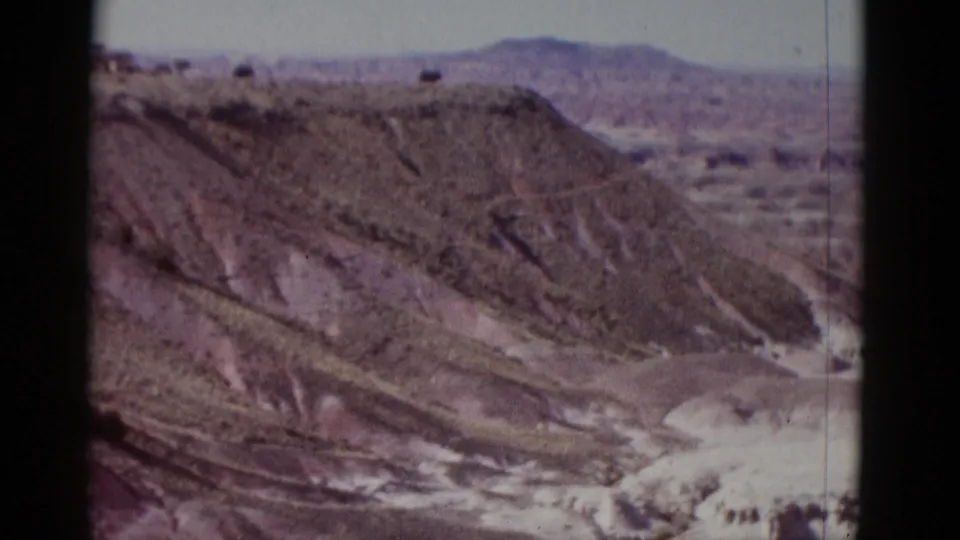 1952 Arizona home-movie frame showing layered desert terrain, pale wash areas, and distant mountains in soft color.