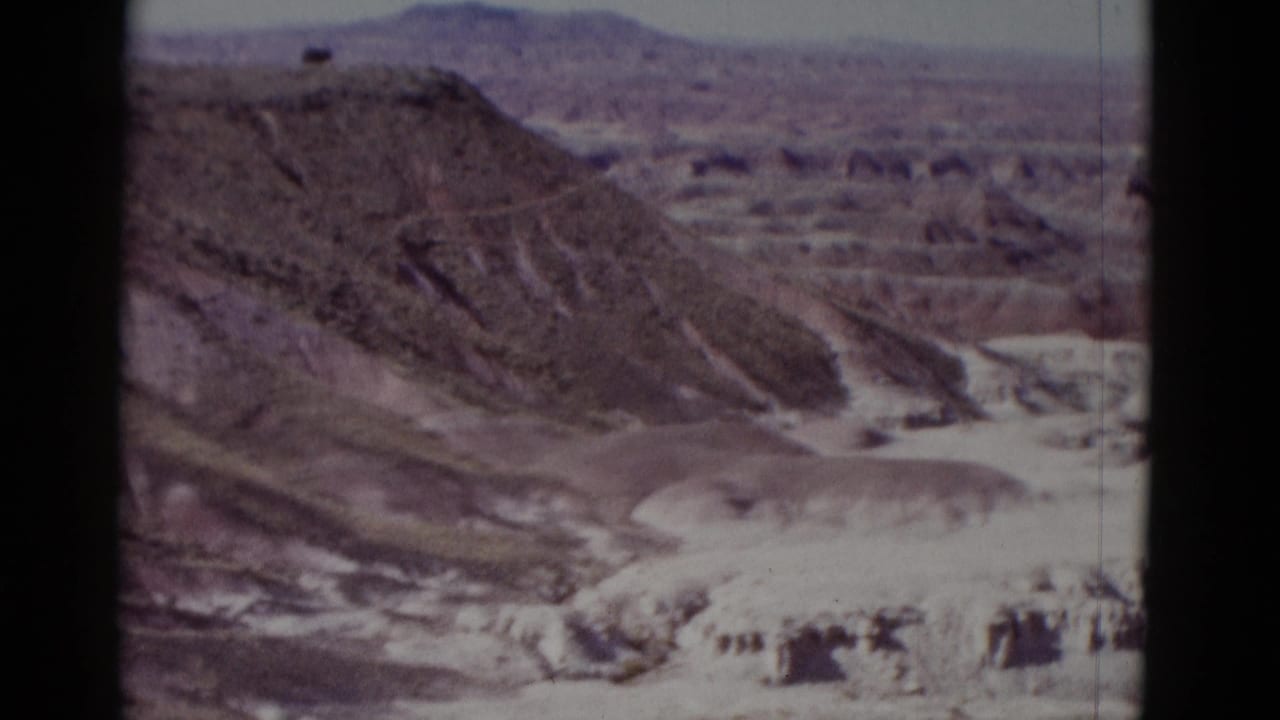 Canyon overlook with layered rock, pale shelves, and a distant arid valley.