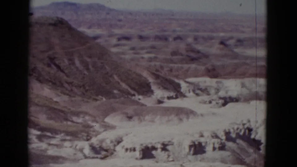 1952 Arizona 8mm frame showing a soft-focus sweep over pale canyon beds, eroded slopes, and distant desert mesas.