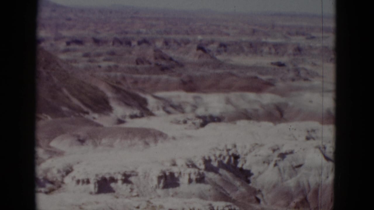 1952 Arizona 8mm frame showing dry canyon terrain, layered ridges, and a hazy horizon with no people or structures visible.