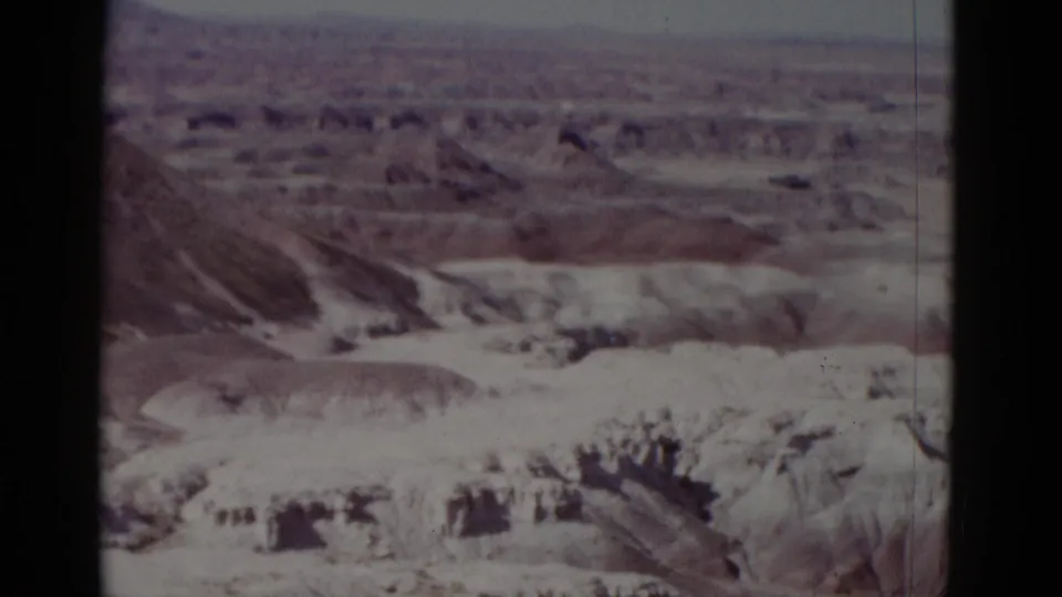 1952 Arizona 8mm frame showing dry canyon terrain, layered ridges, and a hazy horizon with no people or structures visible.