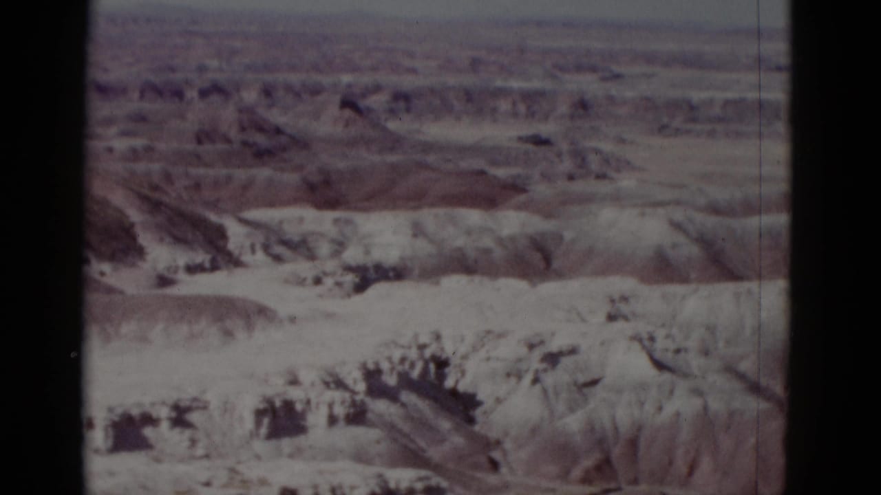 Layered arid terrain with pale slopes, darker ridgelines, and a distant flat horizon.