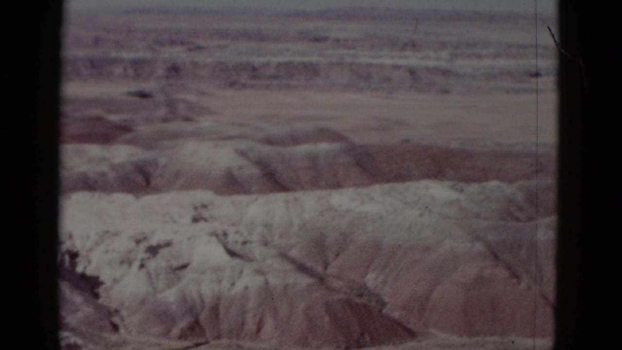 Soft 8mm view of pale desert ridges seen through a dark contact-sheet frame border.