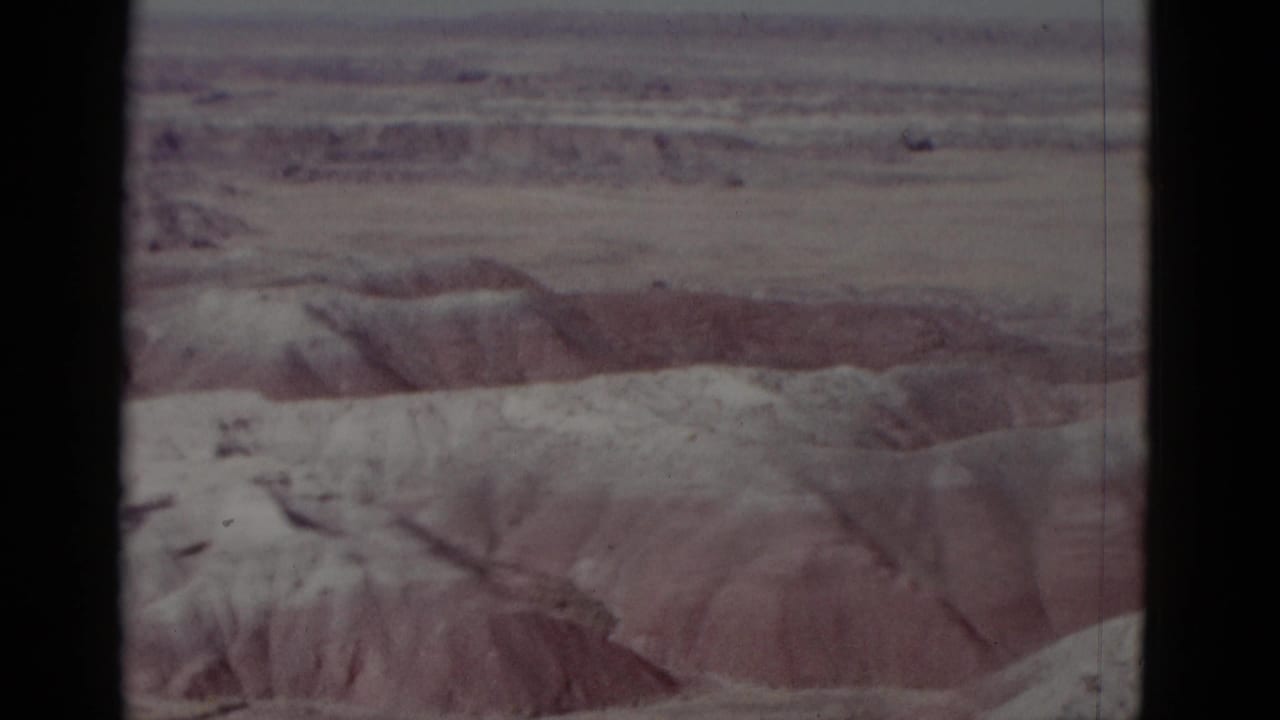Faded desert landscape with eroded ridges and dark contact-sheet borders.