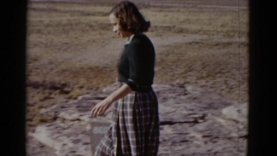 Profile view of a woman walking over sunlit rocky desert ground, supported by metadata as Arizona, 1952.