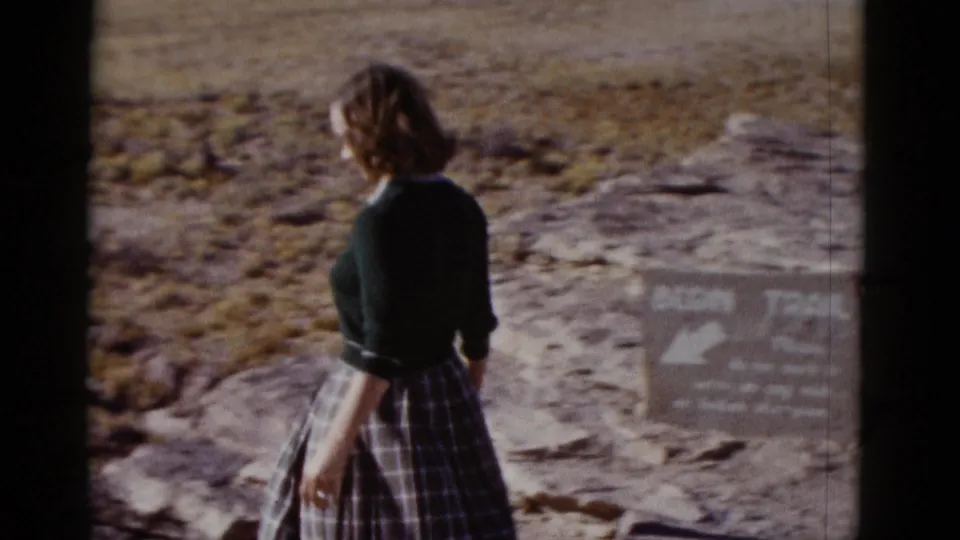 Woman viewed from behind near a weathered trail sign while walking through rocky Arizona desert terrain.