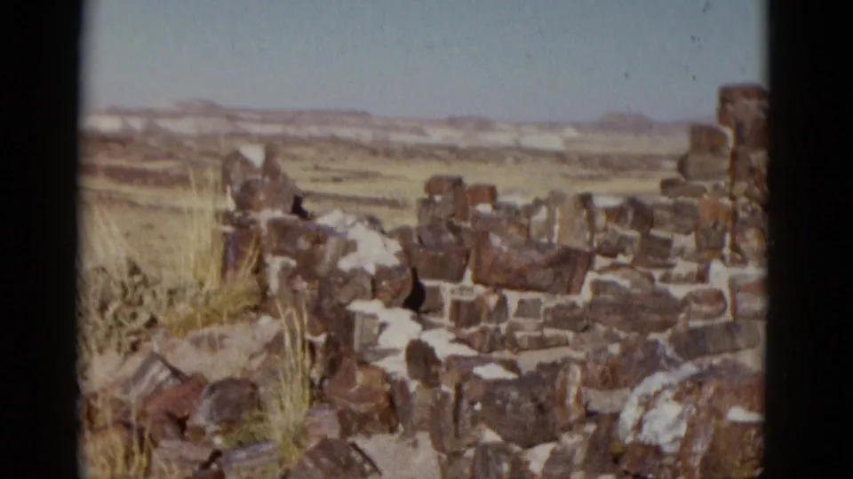 1952 Arizona travel footage frame showing rough stone walls or a rock ruin in open desert with distant low hills.