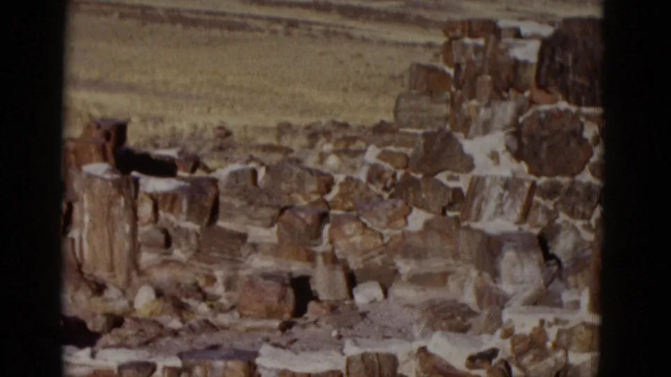 Handheld 8mm frame of a weathered stone wall or rock pile in Arizona desert, with dry ground and open terrain behind it.