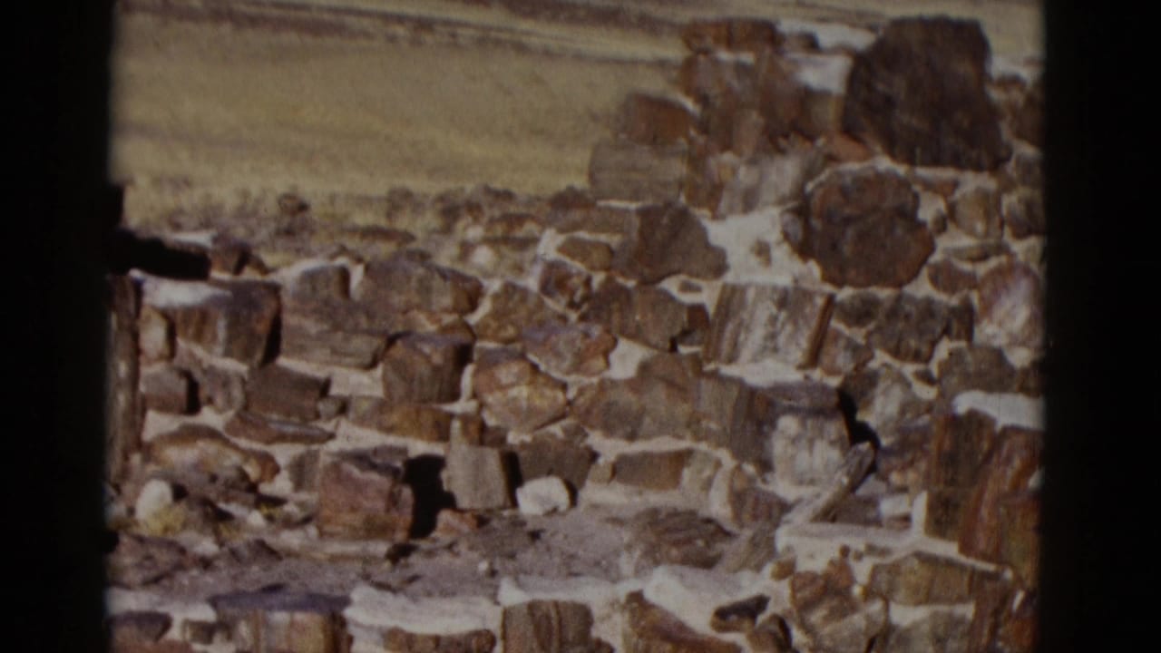 1952 Arizona home-movie frame showing a rough stone wall in bright desert light with open plains and low hills in the distance.