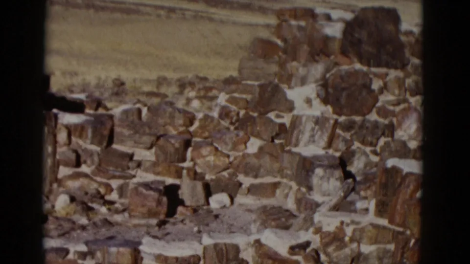 1952 Arizona home-movie frame showing a rough stone wall in bright desert light with open plains and low hills in the distance.