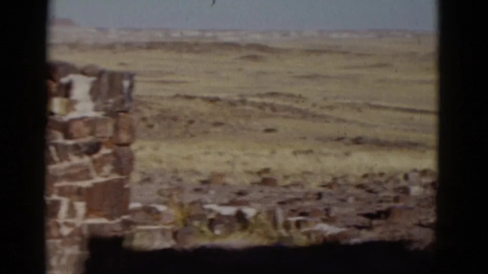 1952 Arizona desert view from beside a stone wall, showing open scrubby ground, distant low hills, and bright sky.