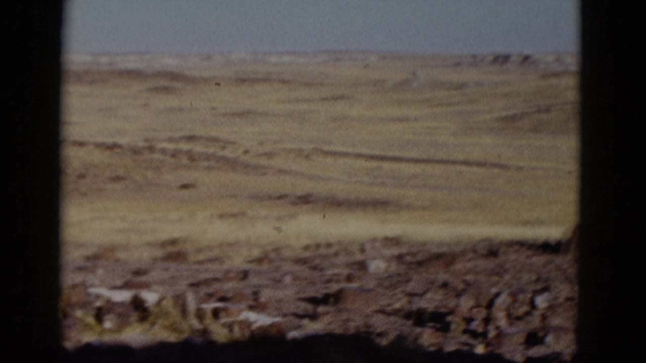 1952 8mm Arizona travel frame showing open grassland, rough rocks in the foreground, distant hills, and dark gate borders.