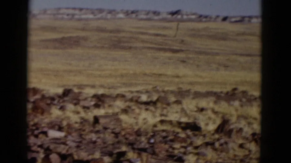1952 Arizona landscape frame with dry grass, scattered rocks, open plain, low hills, and visible 8mm gate edges.