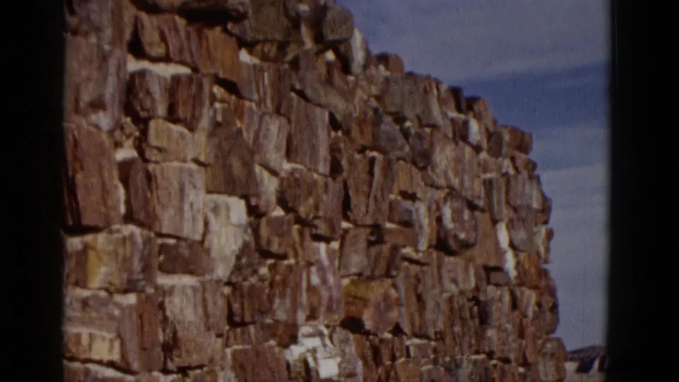 1952 Arizona travel footage frame showing a weathered stone wall of irregular blocks, with sky and distant land at the edge.