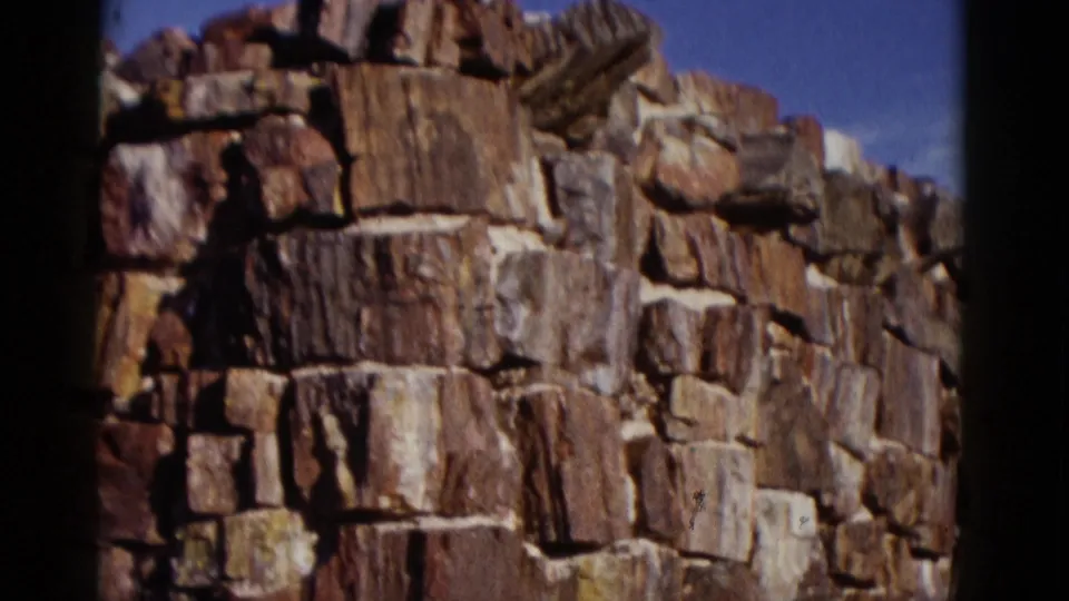 1952 Arizona frame centered on a rough stone wall corner, with irregular rock blocks, pale joints, and dark film-edge shadows.