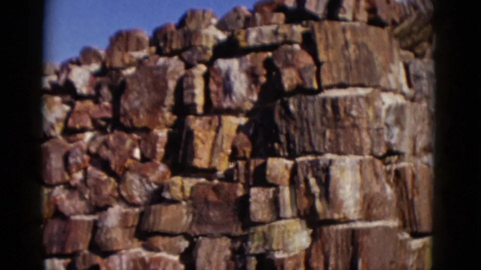 1952 Arizona home-movie frame showing a closer section of rough red-brown stonework at a corner under clear sky.